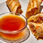 Leckere Frühlingsrollen auf einem Teller mit einer Schale süßer Dipsauce, ideal für asiatische Küche.